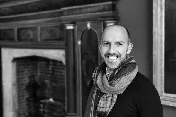 Portrait photograph of Tom Foakes, new SPS Director, standing in an historic interior in front of a fireplace